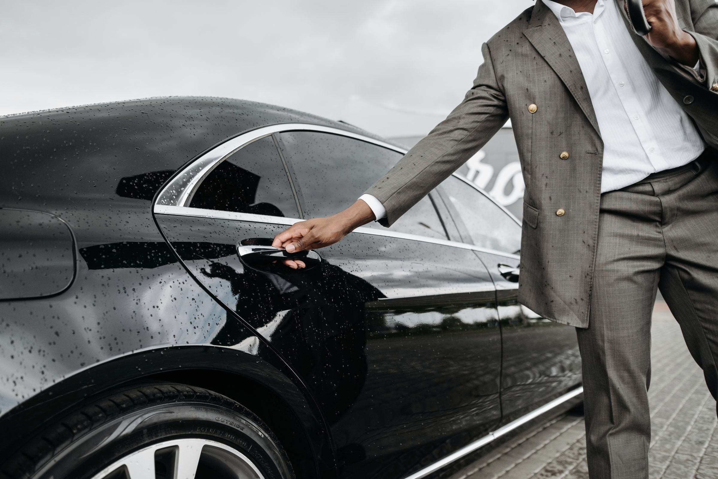 A chauffeur holding the door of a black sedan outside a grand hotel at night